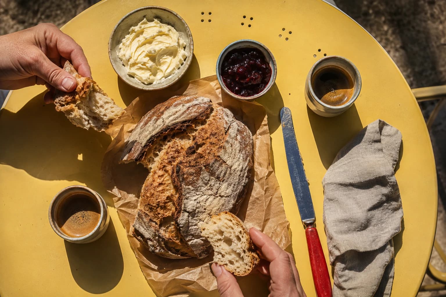 Hands sharing sourdough with whipped butter, cherry jam, and coffee